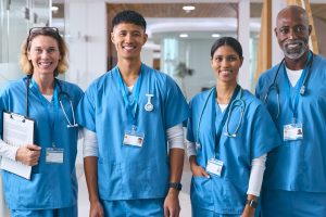 Portrait Of Smiling Multi Cultural Medical Team Wearing Scrubs In Modern Hospital